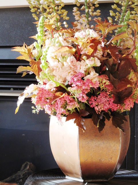 An arrangement of pale colored flowers in a coppery vase