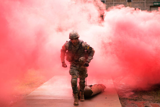 A soldier running out of a plume of red smoke obscuring what is behind him