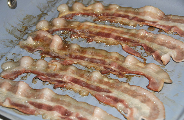 Bacon in a pan showing the color of still chewy bacon