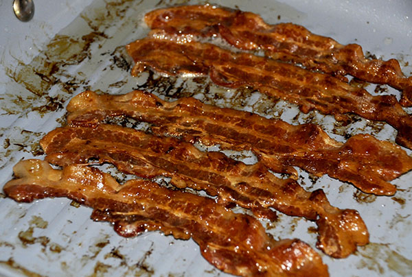 Crispy bacon in a pan shows dark brown red coloring