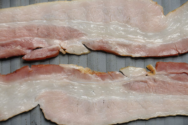 A close-up of raw bacon in a pan showing pale and darker pink coloring