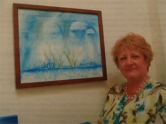 A photograph of artist Iris Hardy standing next to one of her paintings