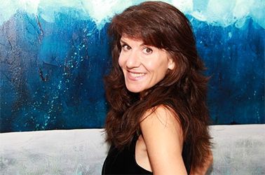 A portrait of artist and color therapy expert Leanne Venier in front of one of her blue and white paintings