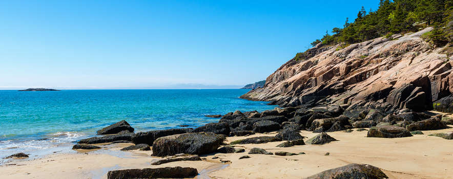 A view from the beach of the crisp blue water, rocky shoreline and soil colors of Acadia National Park