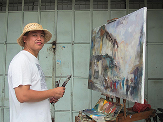 Ng Woon Lam turns to smile at the camera while working on a painting