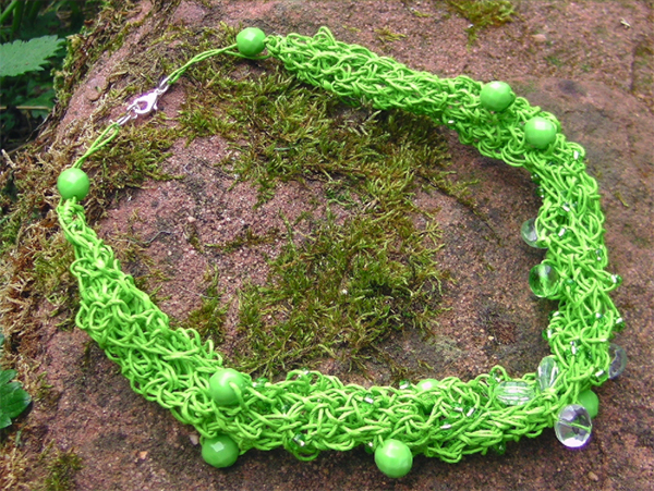 A bright green necklace with woven circles of paper and hanging beads sits on soil