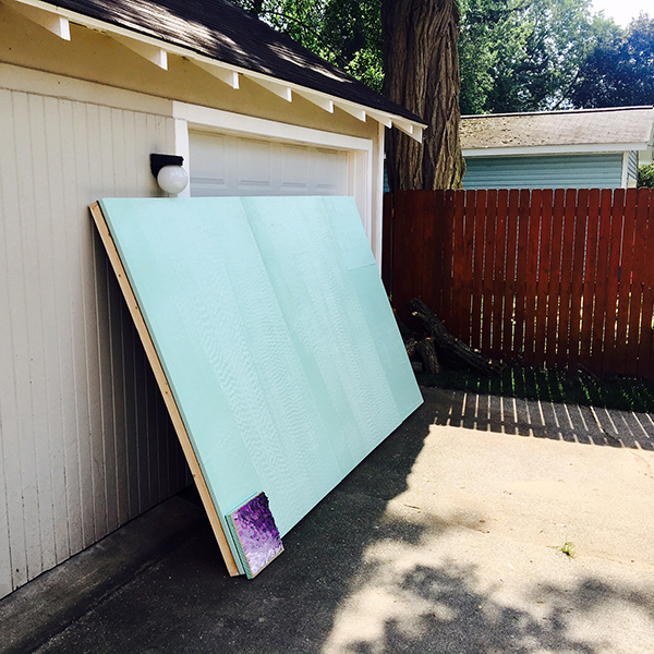 A large wood panel rests against a garage door ready for color chips