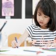 A young kid sits at a desk coloring with crayons