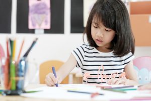 A young kid sits at a desk coloring with crayons